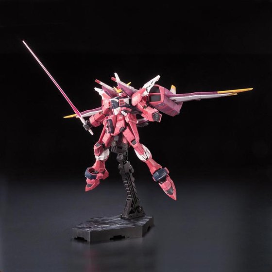 RG Justice Gundam en pose aérea con sable de haz y Fatum-00 desplegado; peana vendida por separado.